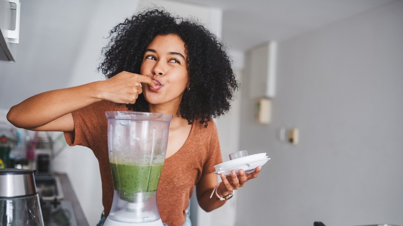 vrouw proeft groene smoothie uit blender